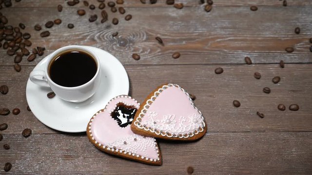 Food art. Good morning concept. cup of coffee and 2 heart-shaped gingersnaps are on wooden background. Coffee beans fall down in slow motion