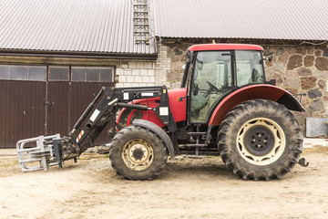 Fototapeta premium Tractor with hydraulic lift for carrying bales of hay and silage. Picture of the side of the agricultural machine. The equipment for a dairy farm.