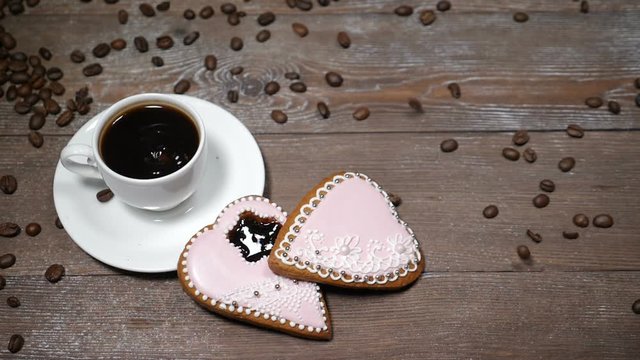 Food art. Good morning concept. cup of coffee and 2 heart-shaped gingersnaps are on wooden background. Coffee beans fall down in slow motion
