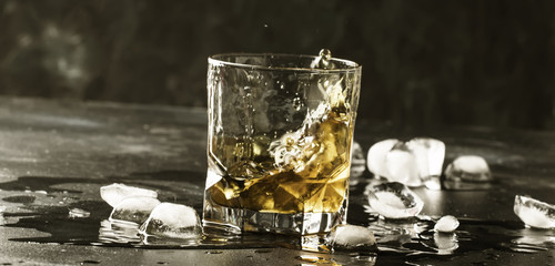Whiskey with ice, splashes out of glass, dark background, toned image, banner, selective focus