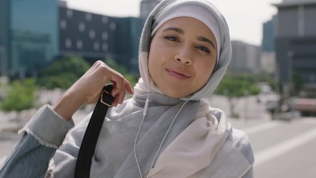 portrait of beautiful young muslim woman student looking confident at camera listening to music using earphones wearing hijab headscarf