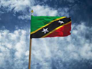 Saint Kitts and Nevis flag Silk waving flag of Saint Kitts and Nevis made transparent fabric with wooden flagpole gold spear on background blue sky white smoke clouds real retro photo 3d illustration