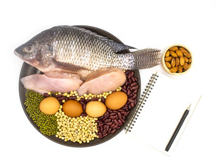 healthy natural food and diet concept - high protein many beans and meat, red beans, green beans, soy beans, egg, chicken and fish in the brown dish isolated on white background with book and pen