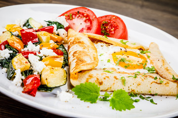 Crepes with eggs on wooden background