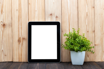 Blank tablet computer and little tree or flower bouquet in white vase on wood background with copy space.