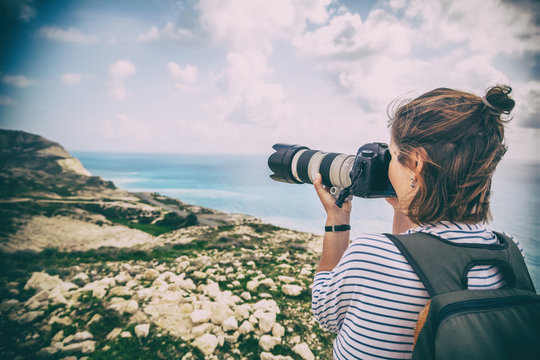 Young woman professional photographer and traveler takes pictures of the landscape on the sea and hills, beautiful nature, profession, vacation and travel concept