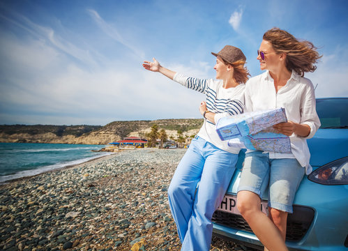 Two young beautiful girls girlfriends traveling together in a car, on the beach on a bright sunny summer day, with map in hand, travel and holidays