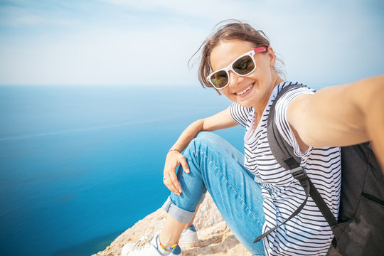 Young beautiful female tourist girl doing selfie on a blue sea background, summer travel and vacation concept, happiness and freedom