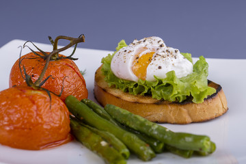 Poached egg on a piece of bread with fried green beans, tomato and arugula on a plate