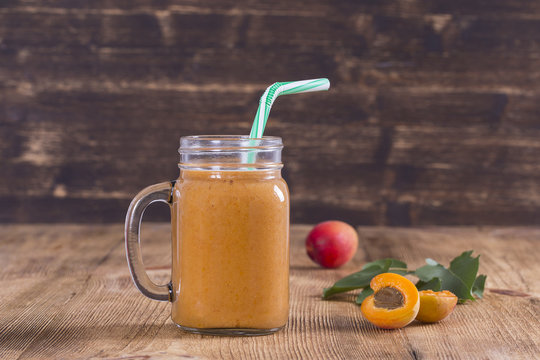 Healthy eating, food, dieting and vegetarian concept - smoothie from apricot and peach in glass mug. Fresh apricot and juice on wooden background