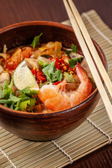 Asian Oriental Cuisine. Japanese spicy soup with seafood, shrimps, vegetables, lime, parsley, and hot pepper, in a plate of red clay, stands on a table in a restaurant. Copy space, selective focus