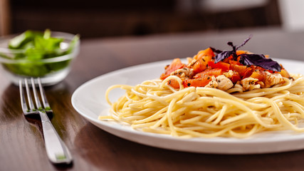 Italian pasta spaghetti with red tomato sauce, tomatoes and grilled chicken. It is on the table in the restaurant. Copy space, selective focus