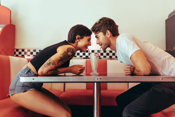 Couple sharing a glass of milk shake at a diner