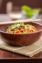 Asian Oriental Cuisine. Japanese noodles with chicken and vegetables, sesame and parsley, in a plate of red clay, stands on a table in a restaurant. Copy space, selective focus