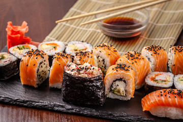 Asian traditional cuisine. A large set of rolls and sushi on a black slate stone, on a wooden table in a restaurant, with soy sauce and Chinese chopsticks.