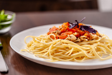 Italian pasta spaghetti with red tomato sauce, tomatoes and grilled chicken. It is on the table in the restaurant. Copy space, selective focus