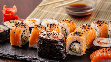 Asian traditional cuisine. A large set of rolls and sushi on a black slate stone, on a wooden table in a restaurant, with soy sauce and Chinese chopsticks.