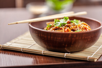 Asian Oriental Cuisine. Japanese noodles with chicken and vegetables, sesame and parsley, in a plate of red clay, stands on a table in a restaurant. Copy space, selective focus