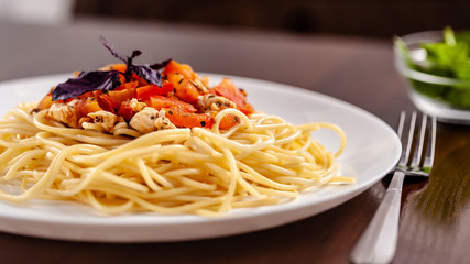 Italian pasta spaghetti with red tomato sauce, tomatoes and grilled chicken. It is on the table in the restaurant. Copy space, selective focus