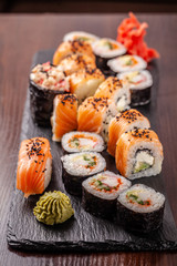 Asian traditional cuisine. A large set of rolls and sushi on a black slate stone, on a wooden table in a restaurant, with soy sauce and Chinese chopsticks.