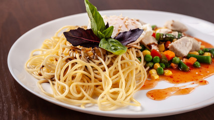 Italian pasta Spaghetti with vegetables and chicken. With red salsa sauce and basil. It is on the table in the restaurant. Copy space, selective focus