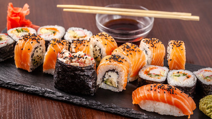 Asian traditional cuisine. A large set of rolls and sushi on a black slate stone, on a wooden table in a restaurant, with soy sauce and Chinese chopsticks.