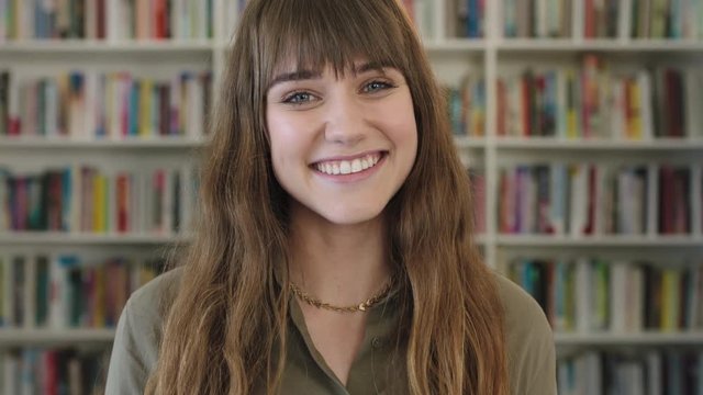 close up portrait of young pretty librarian woman smiling happy looking at camera in library bookshelf background