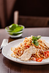 Italian pasta spaghetti with red tomato sauce, tomatoes and grilled chicken. It is on the table in the restaurant. Copy space, selective focus