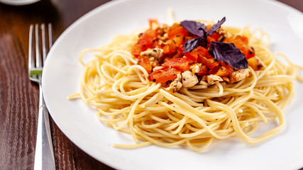 Italian pasta spaghetti with red tomato sauce, tomatoes and grilled chicken. It is on the table in the restaurant. Copy space, selective focus