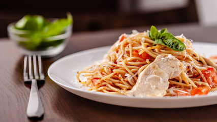 Italian pasta spaghetti with red tomato sauce, tomatoes and grilled chicken. It is on the table in the restaurant. Copy space, selective focus