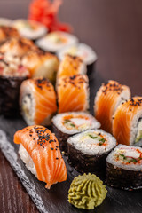Asian traditional cuisine. A large set of rolls and sushi on a black slate stone, on a wooden table in a restaurant, with soy sauce and Chinese chopsticks.