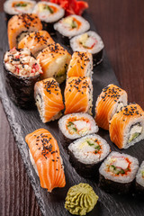Asian traditional cuisine. A large set of rolls and sushi on a black slate stone, on a wooden table in a restaurant, with soy sauce and Chinese chopsticks.