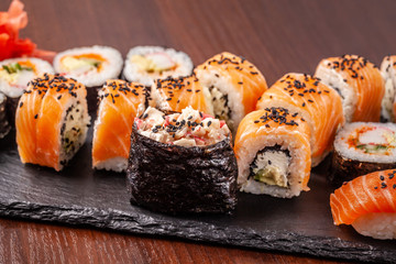 Asian traditional cuisine. A large set of rolls and sushi on a black slate stone, on a wooden table in a restaurant, with soy sauce and Chinese chopsticks.