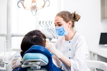 Dentist in a white coat treats the girl's teeth on professional equipment