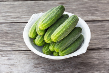 whole green cucumbers in a large white antique plate on a wooden table
