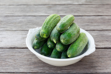 whole green cucumbers in a large white antique plate on a wooden table