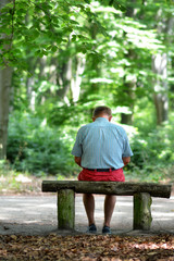 Trauriger Mann allein auf Bank in Wald