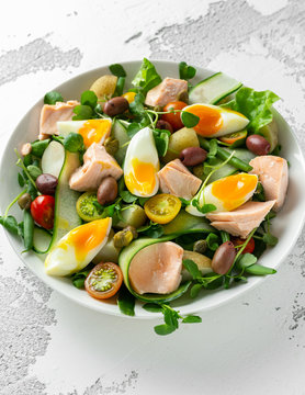 Healthy Nicoise salad with salmon, colourful sweet cherry tomatoes, olives, green beans, cucumber ribbons, soft boiled eggs, water-cress leaves with Mediterranean seasoning