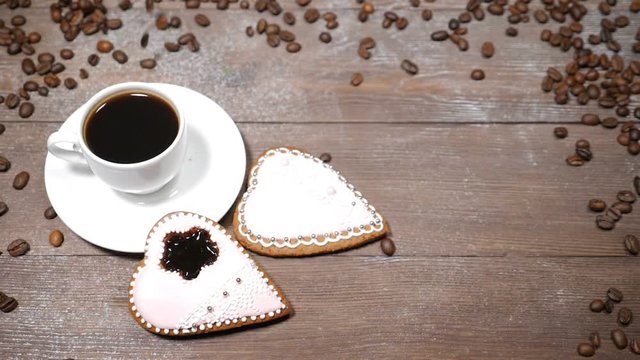 Food art. Good morning concept. cup of coffee and 2 heart-shaped gingersnaps are on wooden background. Coffee beans fall down in slow motion