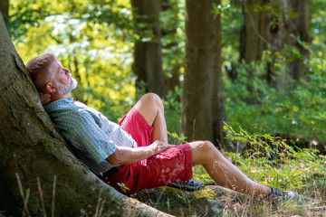 Älterer Mann liegt am Baum in der Sonne