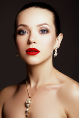 Beauty Brunette Woman with Perfect Makeup. Beautiful Professional Holiday Make-up. Red Lips, perfect eyebrows. Beauty Girl's Face. Gold earrings with pearls and diamonds