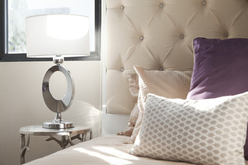 luxury lamp on a beige table beside the bed with a frame headboard and pillow on a bed and curtain in bedroom with light from window. © bennnn