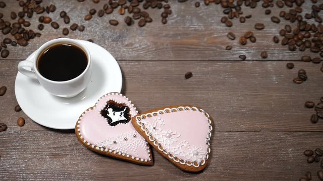 Food art. Good morning concept. cup of coffee and 2 heart-shaped gingersnaps are on wooden background. Coffee beans fall down in slow motion