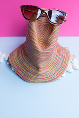 A women's sunglasses over a large sea-bream and several smaller shells on a light blue and fuchsia...