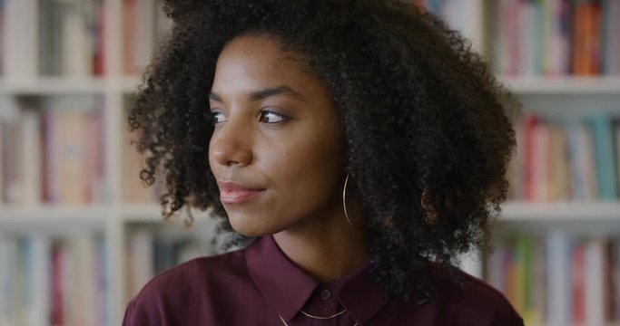 portrait young beautiful african american woman student looking pensive turns head black female with afro hairstyle slow motion bookshelf background