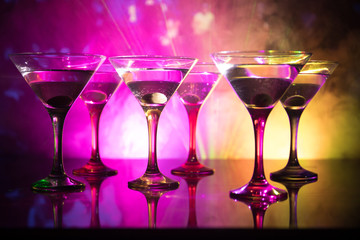 Several glasses of famous cocktail Martini, shot at a bar with dark toned foggy background and disco lights. Club drink concept
