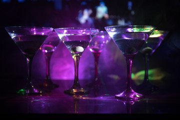 Several glasses of famous cocktail Martini, shot at a bar with dark toned foggy background and disco lights. Club drink concept