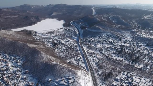 Aerial Vladivostok serpentine nature road traffic car journey mountains hills old buildings village rooftops countryside Lake frozen. Horizon General plan from great height. Winter snow sun day. Done 