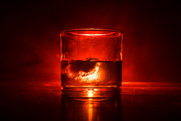 Glass of whiskey and ice on wooden surface with color light and fog on background. Copy space....