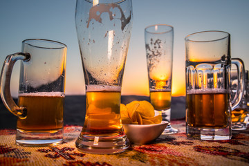 Close up empty mugs of beer on a sunrise background with mountains. Beer party is over concept.